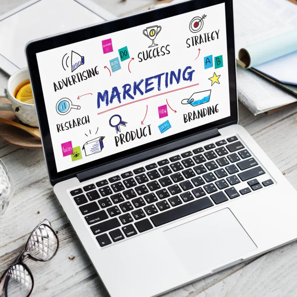 Notebook mostrando o termo “Marketing” com ícones de estratégia, sucesso, produto, pesquisa, marca e publicidade — conceito visual de marketing digital.